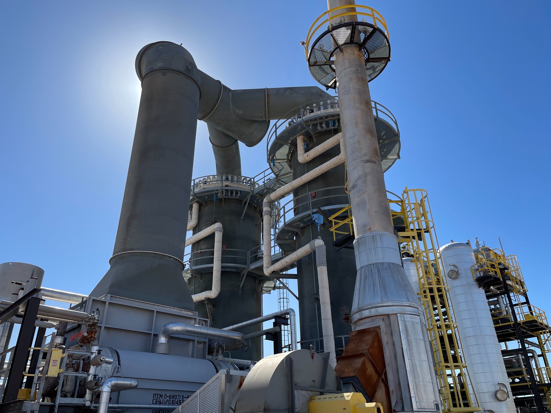 The electrified steam methane reformer: two large vertical reformer vessels with ducting and stacks against a clear sky