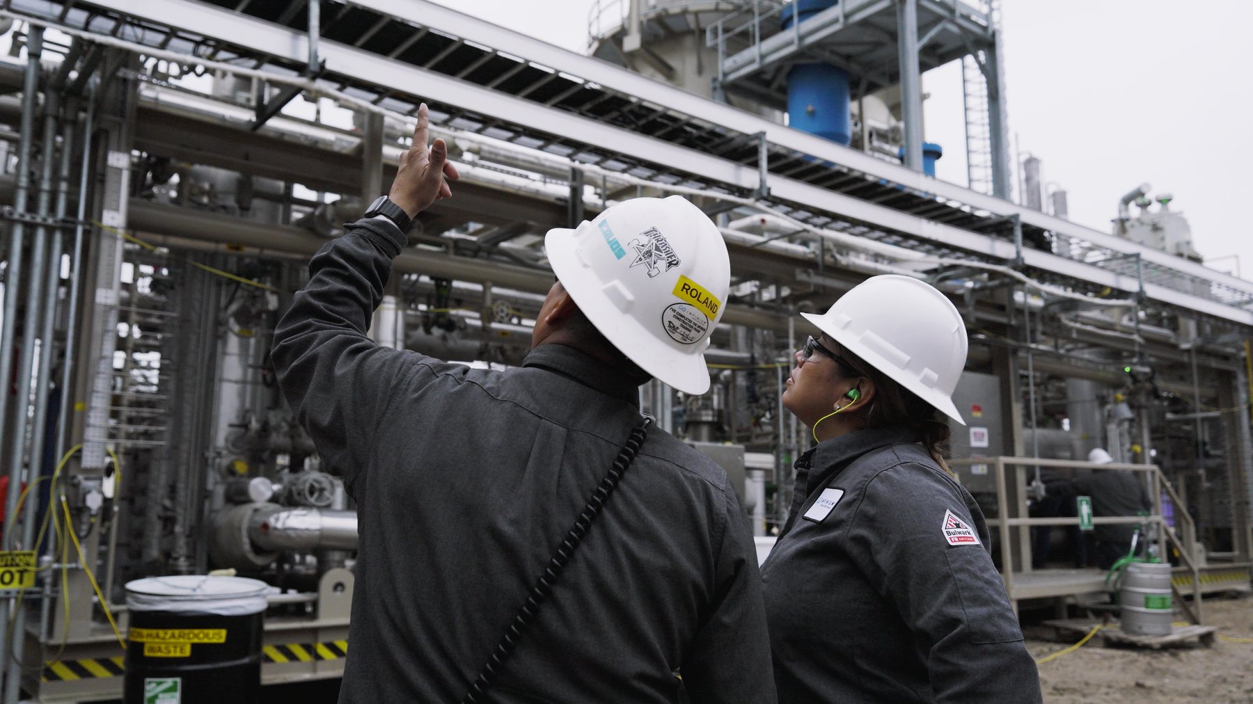 Two Infinium operators in flame-resistant clothing looking up at the Pathfinder process structure